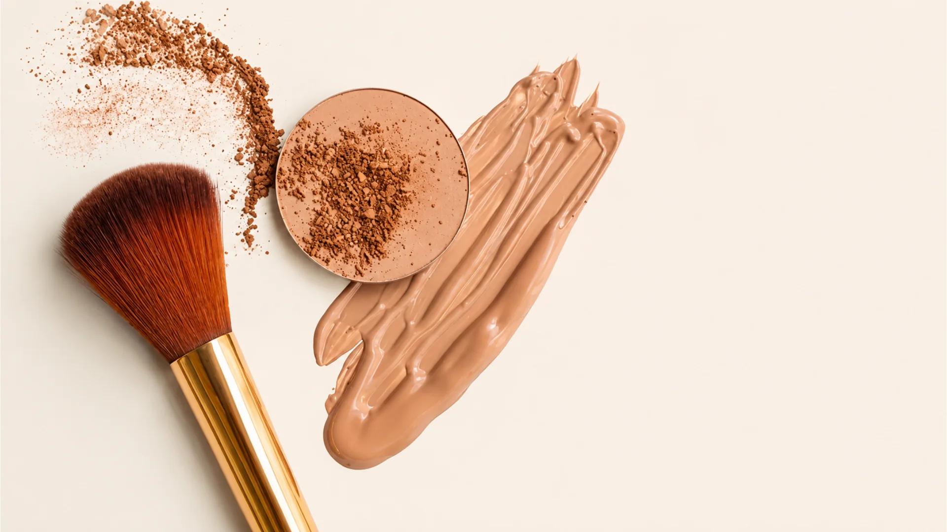 A gold makeup brush beside pressed powder and a foundation swatch